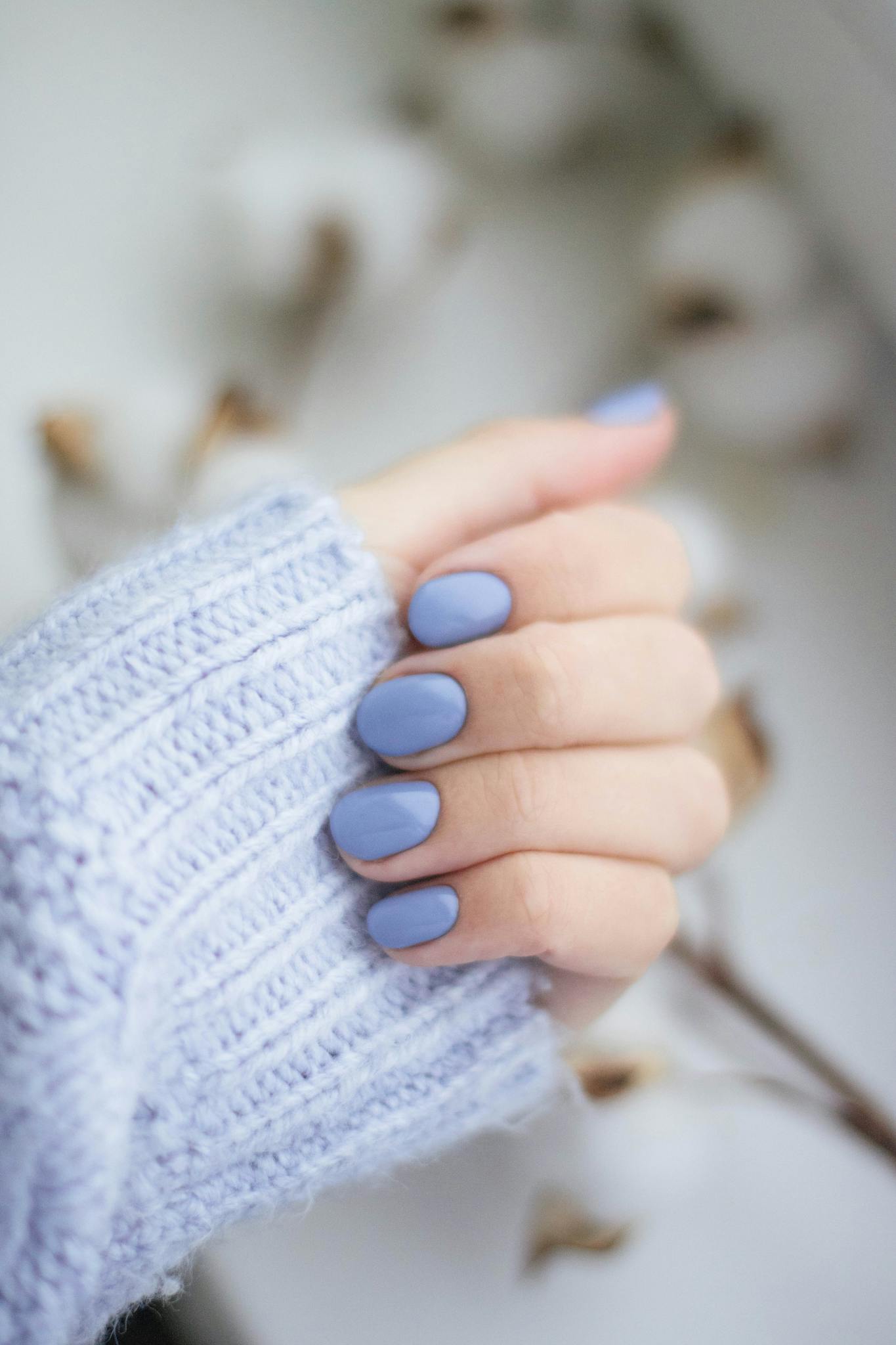 A close-up of a woman's hand with purple manicured nails and knitwear, showcasing trendy fashion.