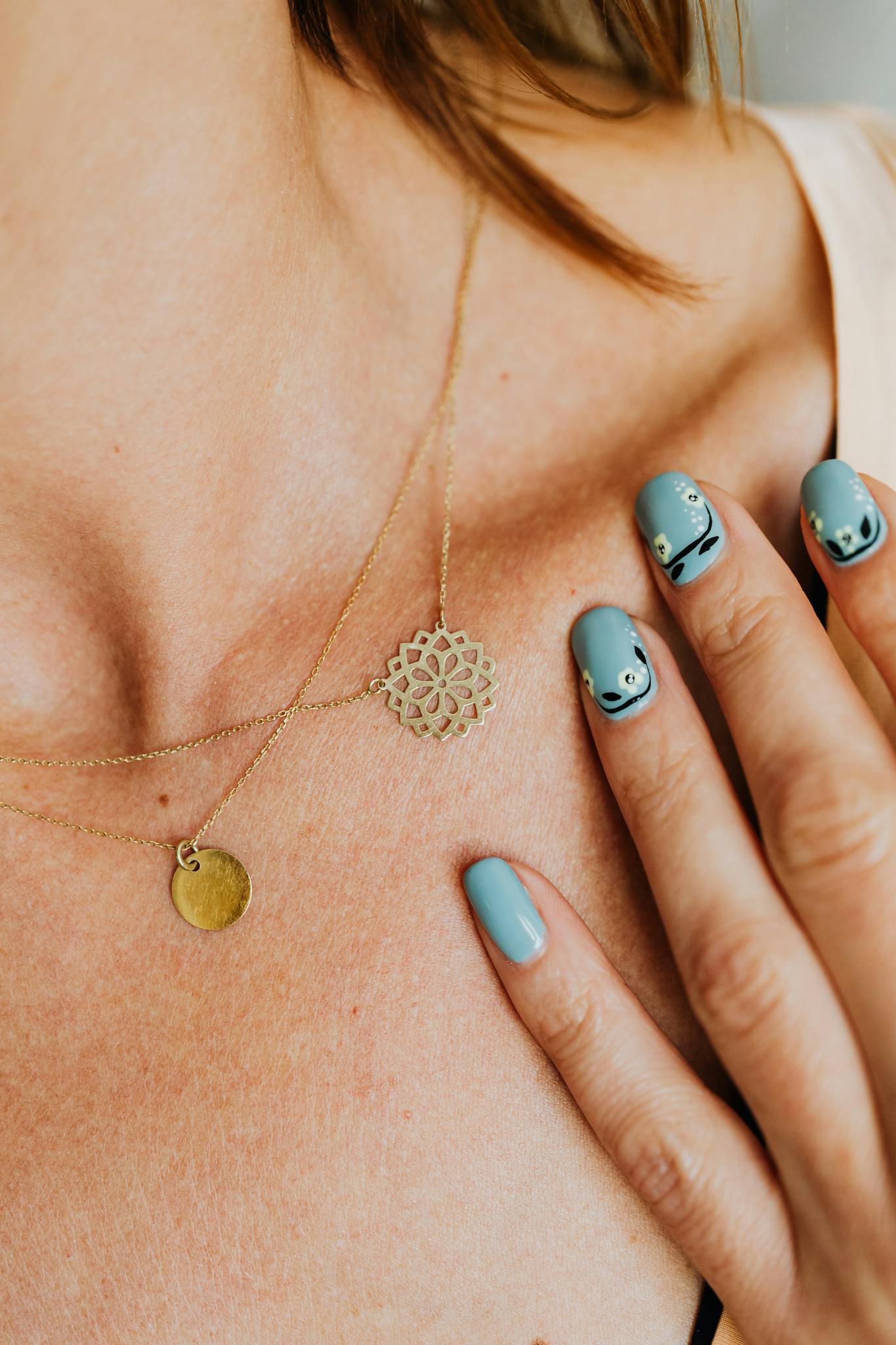 Close-up of a gold necklace with elegant nail art featuring pastel blue tones.